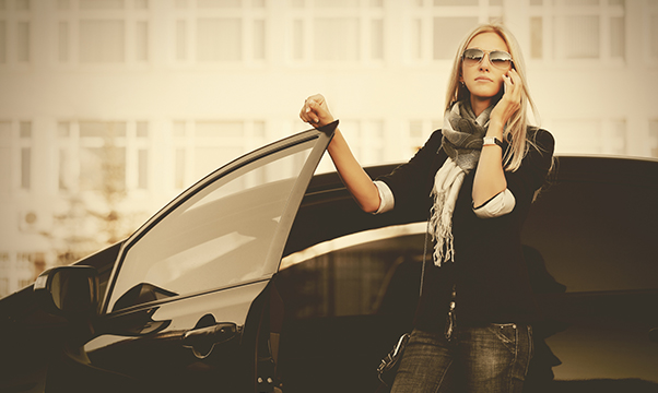 Fashion business woman talking on mobile phone beside a her car Stylish female model in black blazer and sunglasses outdoor